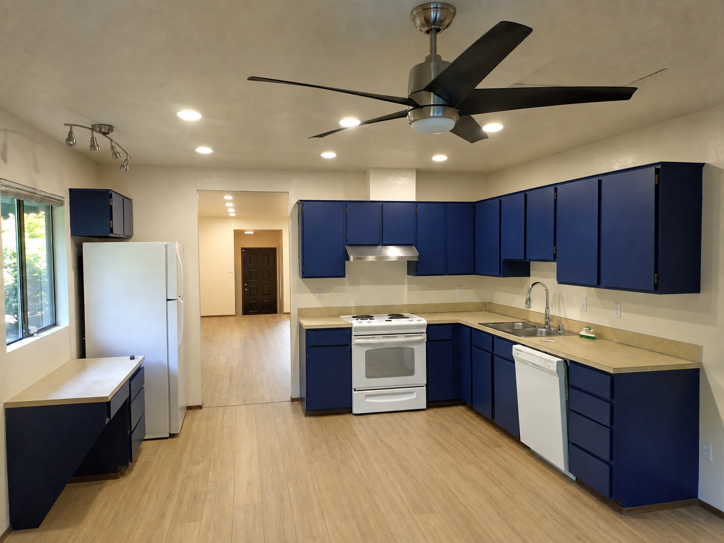 Kitchen after remodel — navy blue painted cabinets, LVP flooring, lifted ceiling with new recessed lighting and ceiling fan