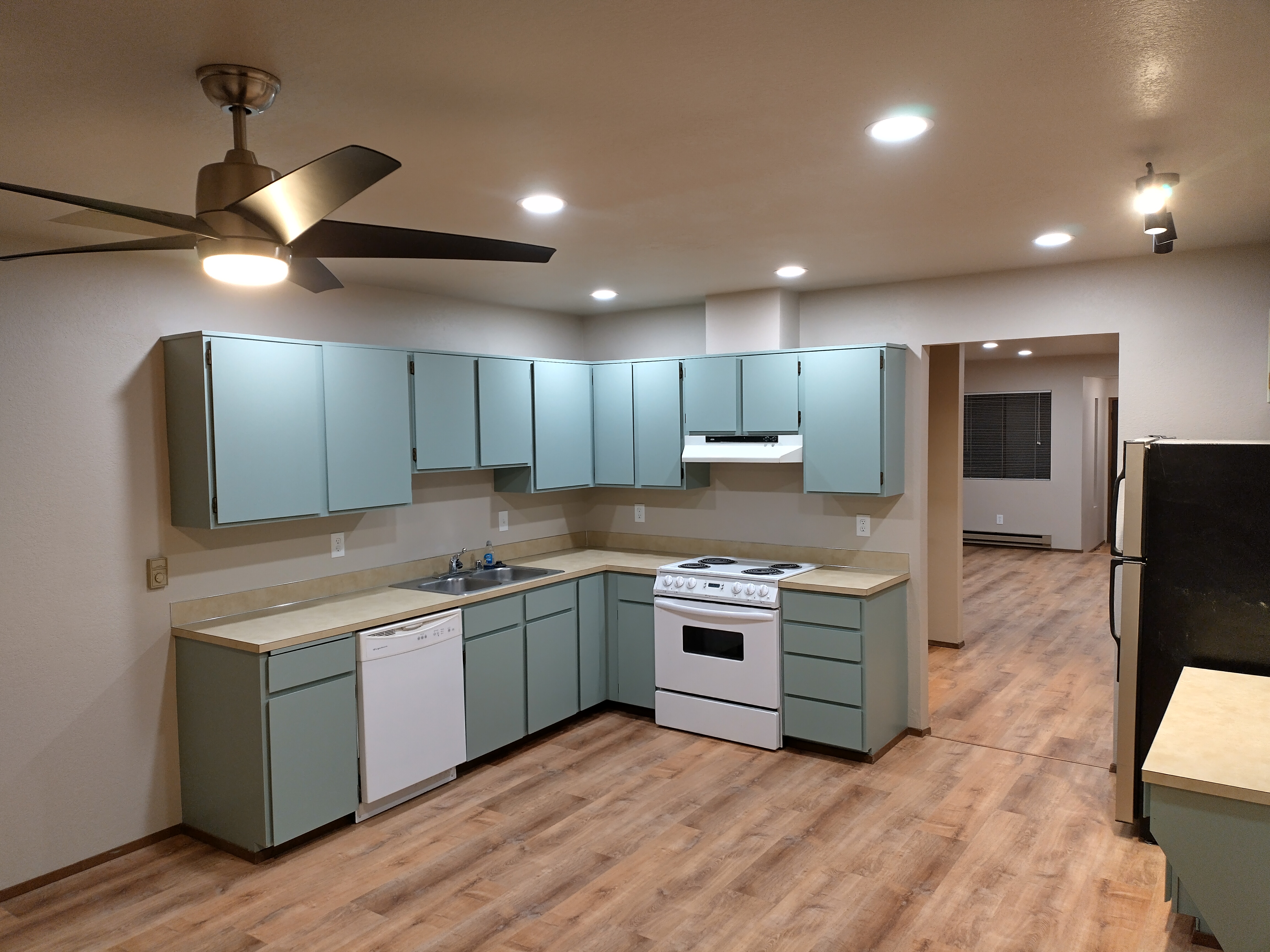 Kitchen after remodel — teal painted cabinets, LVP flooring, lifted ceiling with new recessed lighting and ceiling fan